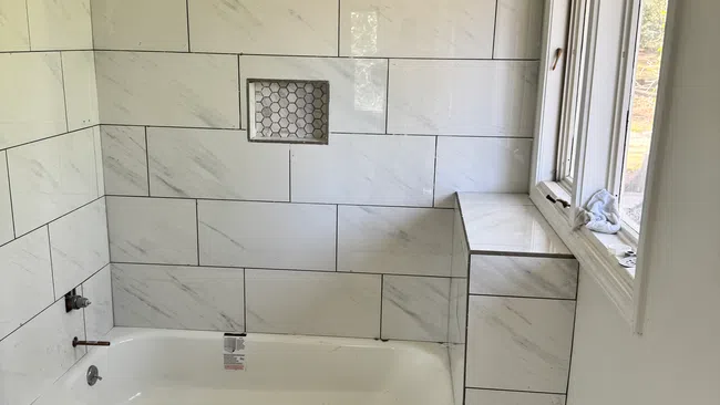 Modern bathroom with white marble wall tiles, hexagonal floor tiles, built-in bathtub, and window natural light.