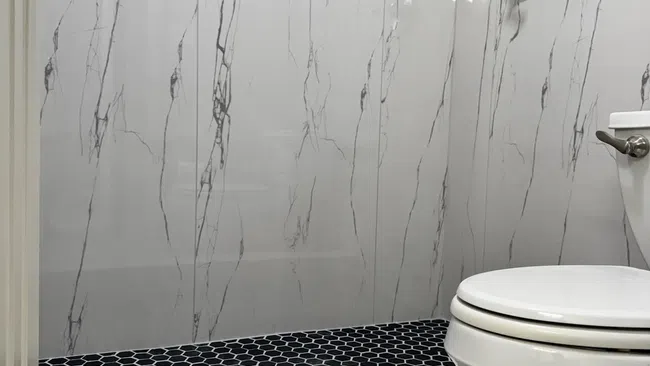 Clean modern bathroom with white marble walls, black hexagonal shower floor tiles, and a white toilet.