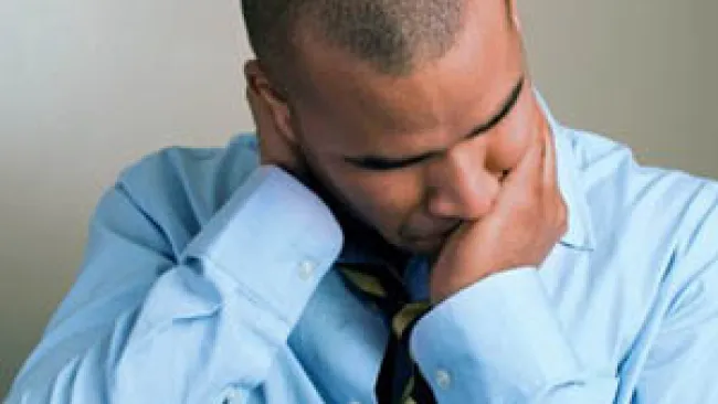 Man in blue shirt and striped tie holding his neck appearing stressed or in pain against a plain background