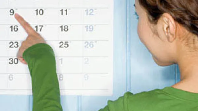 Woman in green pointing at the date 9 on a wall calendar with blue background