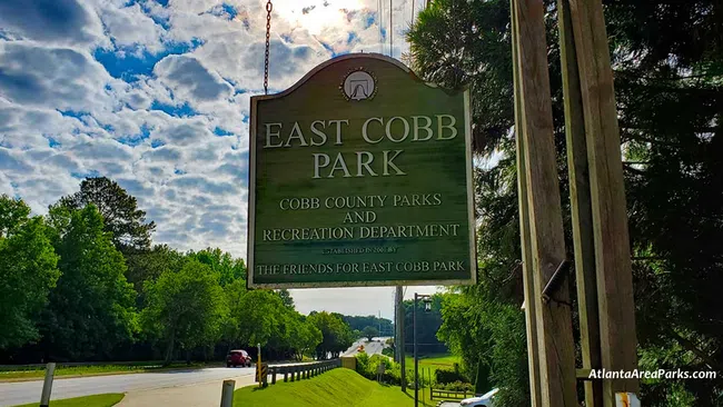 Green wooden sign for East Cobb Park by Cobb County Parks and Recreation under a bright cloudy sky