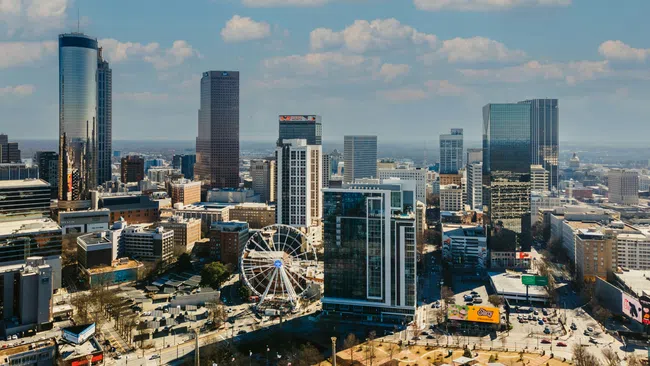 Downtown cityscape with modern skyscrapers, observation wheel, park, and blue sky with scattered clouds