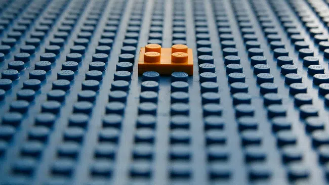 Orange LEGO brick placed on a field of blue LEGO baseplates creating a contrast in color and texture.