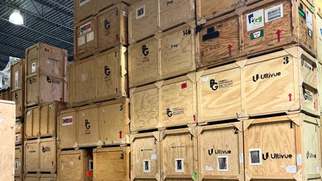 Large wooden shipping crates stacked in a warehouse with company logos and handling labels visible