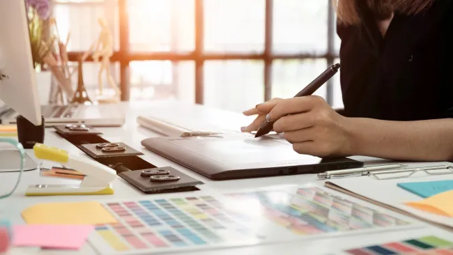 Person using digital pen on graphic tablet at workspace with color swatches and sticky notes