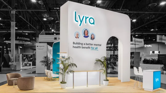 Modern Lyra mental health booth with clean design, light wood flooring, plants, and comfortable seating in expo hall