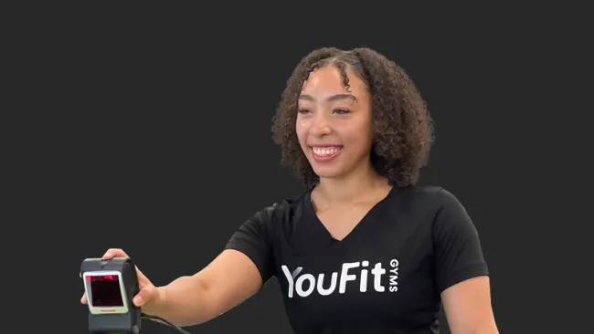 Smiling woman in a YouFit Gyms shirt holding a barcode scanner against a dark background