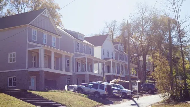 Newly constructed two-story townhouses with front porches on a sunny residential street with parked vehicles.