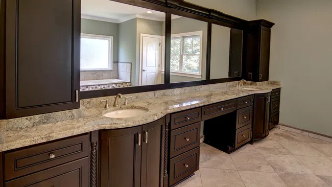 Luxury bathroom vanity with dark wood cabinets, marble countertop, large mirror, and tiled floor under natural light.