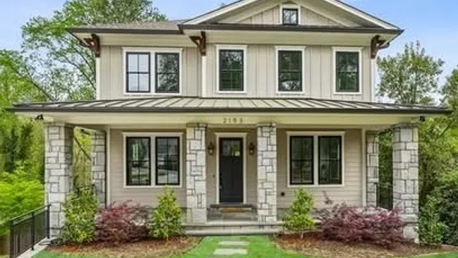 Two-story modern farmhouse with stone pillars, large windows, and a manicured front lawn with stepping stones.
