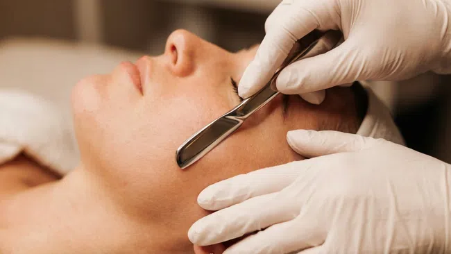 Close-up of facial shaving with a straight razor by a gloved professional on a relaxed client.