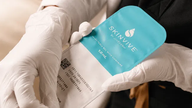 Hands in gloves holding SKINVIVE injectable gel with lidocaine 1.0 mL for skin treatment.