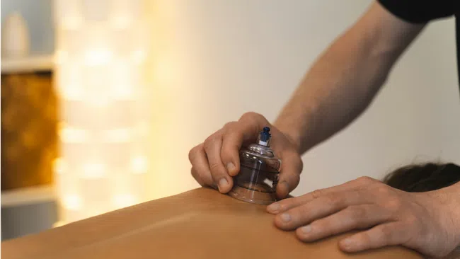 Therapist applying a cupping therapy cup on a patient's back for muscle relief in a warm, softly lit room.