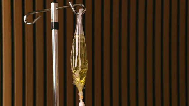 Close-up of an intravenous IV drip bag filled with yellow fluid hanging on a metal stand against a wooden panel background