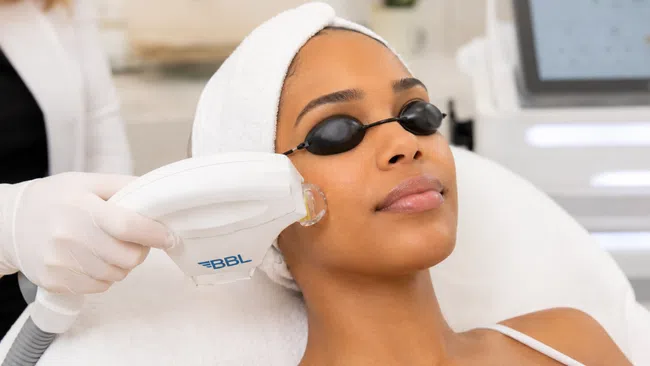 Woman with a towel on her head receiving BBL skin treatment wearing protective eye goggles.