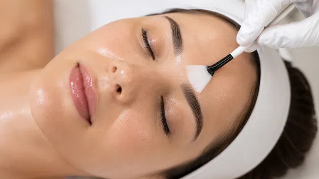 Woman receiving a gentle facial brush treatment with closed eyes and smooth skin in a spa setting.