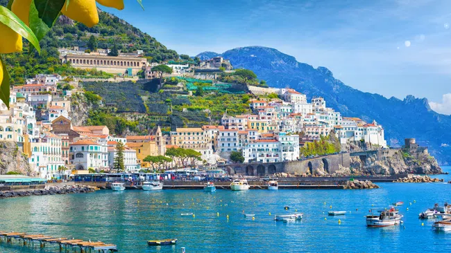 Scenic Amalfi Coast with colorful cliffside buildings, boats in turquoise water, and lemon tree branches in foreground
