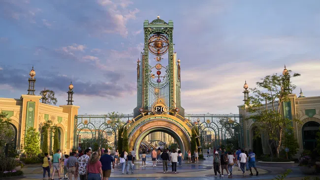 Epic Universe entrance archway with intricate designs and visitors walking under golden light at sunset.