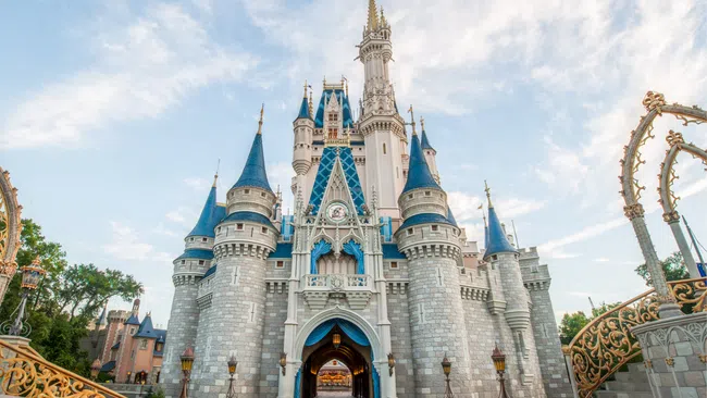View of Cinderella's castle with blue spires under a partly cloudy sky at a theme park entrance.