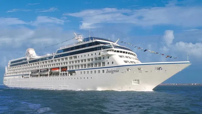 Large white cruise ship Insignia sailing on calm blue ocean under a partly cloudy sky.
