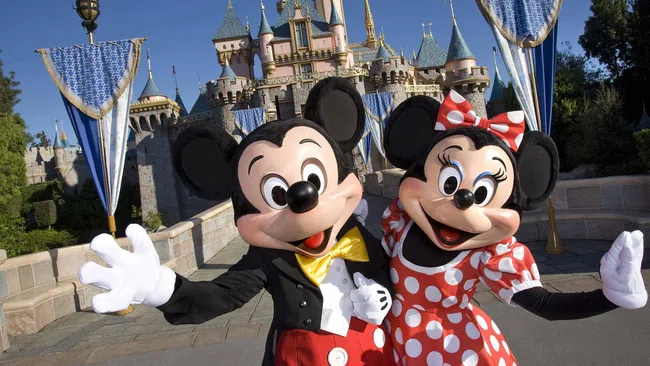 Mickey and Minnie Mouse posing happily in front of Sleeping Beauty Castle at Disneyland on a sunny day.
