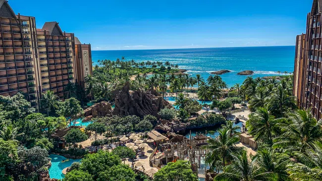 Resort with tropical pools, palm trees, and ocean view under clear blue sky between hotel buildings