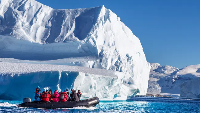 Group of people in a boat exploring massive icebergs in clear blue Arctic waters under a sunny sky