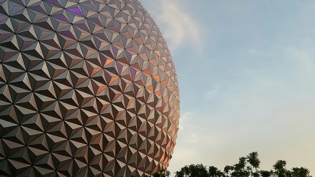 Epcot's iconic geodesic sphere at sunset with sky and silhouetted trees in the foreground.