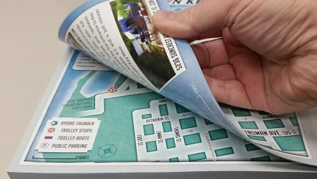 A hand flipping through a colorful, detailed map highlighting routes and local landmarks.
