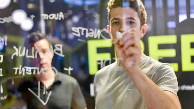 Two men brainstorming with notes on a transparent board in a modern office environment.