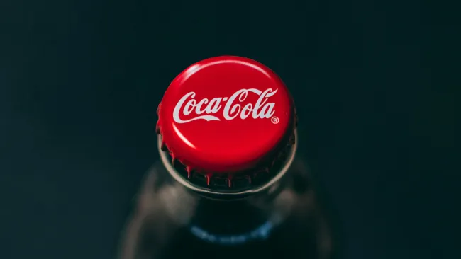 Close-up of a Coca-Cola bottle with a red cap and white logo on a dark background.