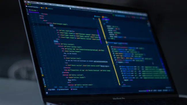 Laptop screen displaying colorful HTML and JavaScript code in a dark-themed development environment.