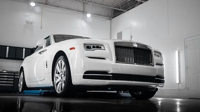 White luxury Rolls-Royce car parked inside a clean, modern garage with bright lighting and reflective floor.