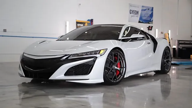 White luxury sports car with black accents and red brake calipers parked indoors on reflective floor.