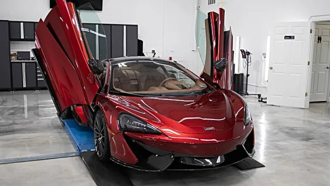 Red sports car with butterfly doors open inside a modern garage with concrete floors and black cabinets.