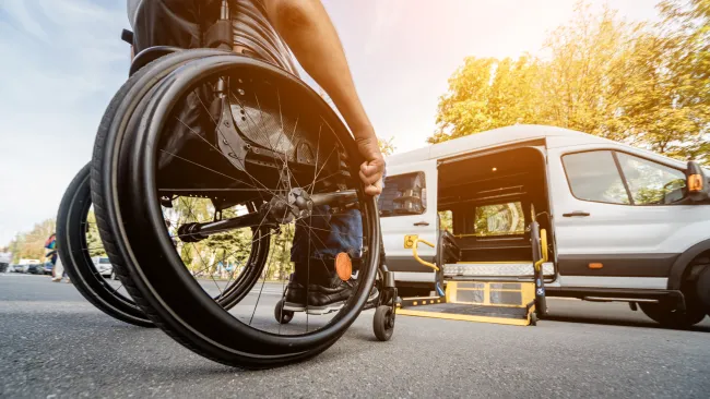 Person in wheelchair approaching accessible van with ramp on sunny day outdoors