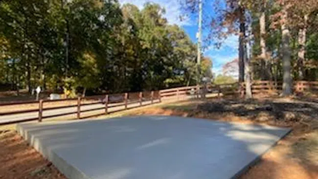 Newly poured concrete slab foundation in a wooded area under a clear blue sky with autumn trees.