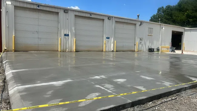 Freshly poured concrete slab in front of industrial garage doors with caution tape around the area.
