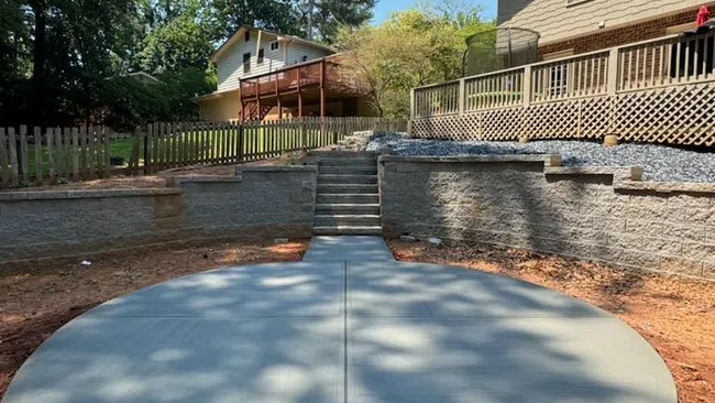 Newly poured concrete pad in a backyard, surrounded by trees and houses under a clear blue sky.