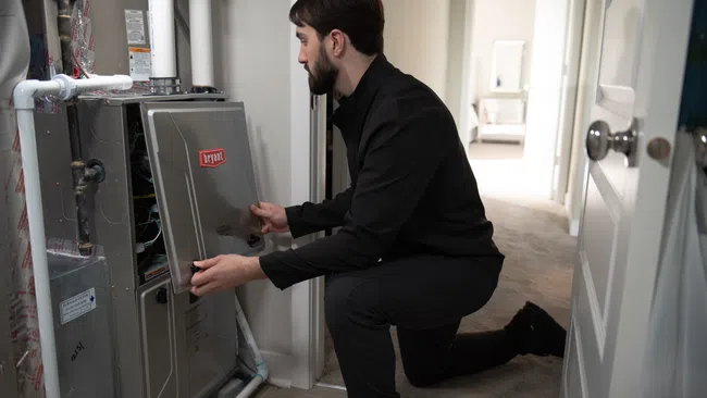 Technician inspecting and opening a Bryant HVAC unit inside a residential home hallway.