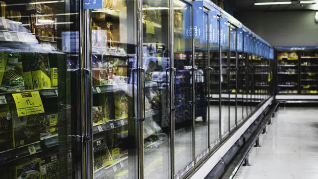 Aisle of refrigerated glass doors displaying frozen foods in a well-lit grocery store aisle.