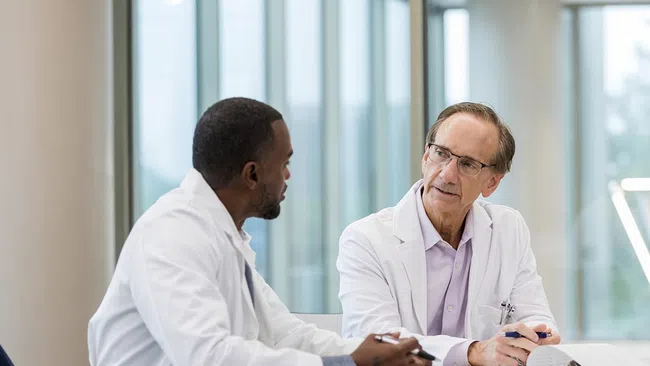 Dentist in white coat explaining a dental model to a patient in a modern office with brick wall background