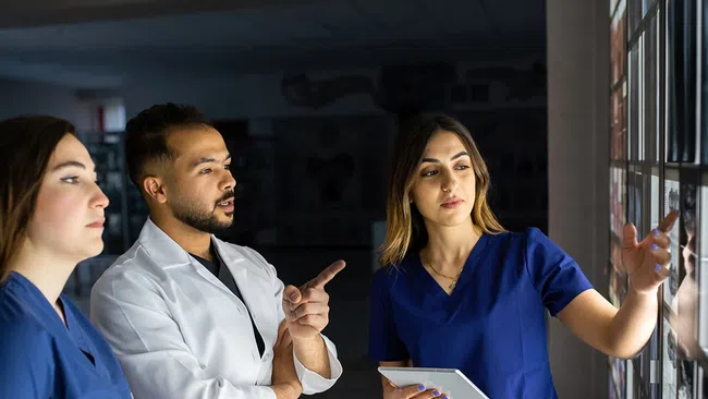 Two doctors in white coats analyzing brain scan images on dual computer monitors in a bright office.