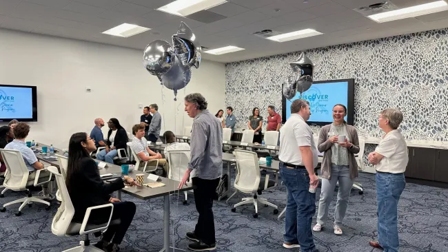 People networking and conversing in a modern conference room decorated with silver balloons and patterned wall design.