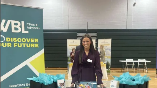 Woman standing behind WBL CPAs and Advisors booth with promotional materials and gift bags at event.