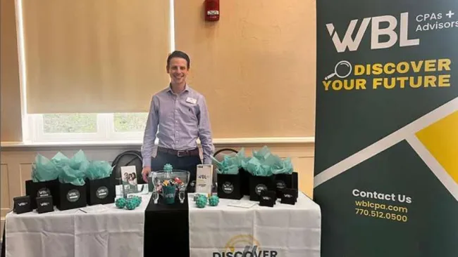 Man standing behind a WBL CPAs and Advisors booth with promotional items and banners at an event.