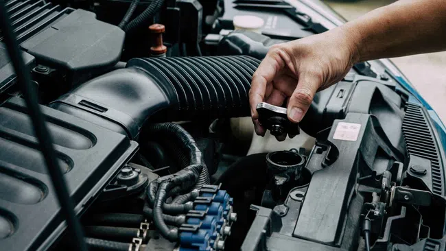 Hand inspecting car engine components with focus on air intake hose and radiator cap under open hood.