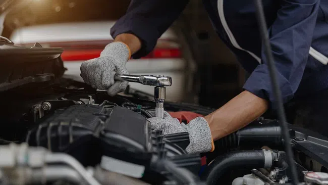 Mechanic wearing gloves using a ratchet wrench to repair a car engine under the hood