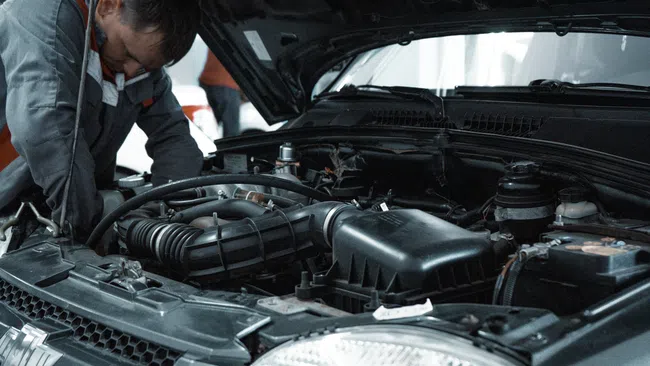 Mechanic inspecting a car engine under the raised hood in an auto repair shop.