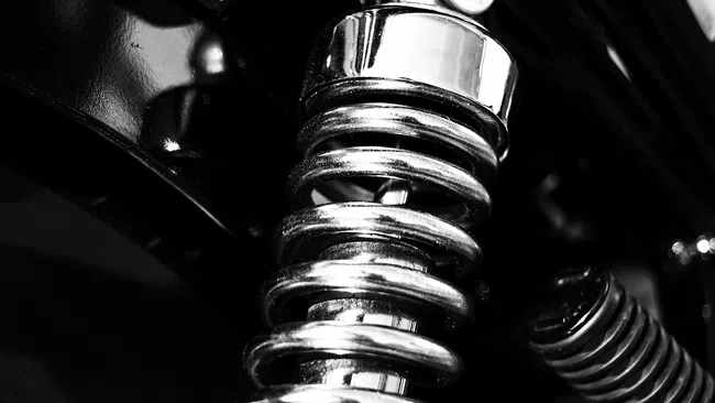 Close-up of a shiny metallic coil spring on a black mechanical suspension system in monochrome.
